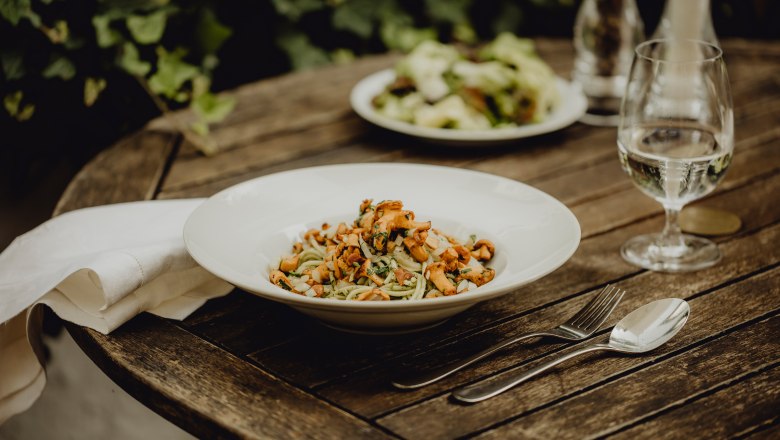 A plate of pesto chanterelle pasta on a wooden table, cutlery and a glass of water next to it.