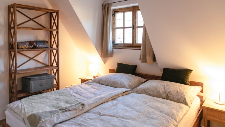 Cozy bedroom with double bed, wooden bookshelf and window with curtains.