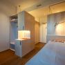 Modern, minimalist hotel room with single bed, wooden floor and desk lamp.