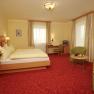 A cozy hotel room with a double bed, sofa, table and TV. Yellow walls and red carpets dominate the room.