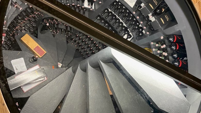 View through a glass panel of a spiral-shaped wine cellar with many bottles of wine.