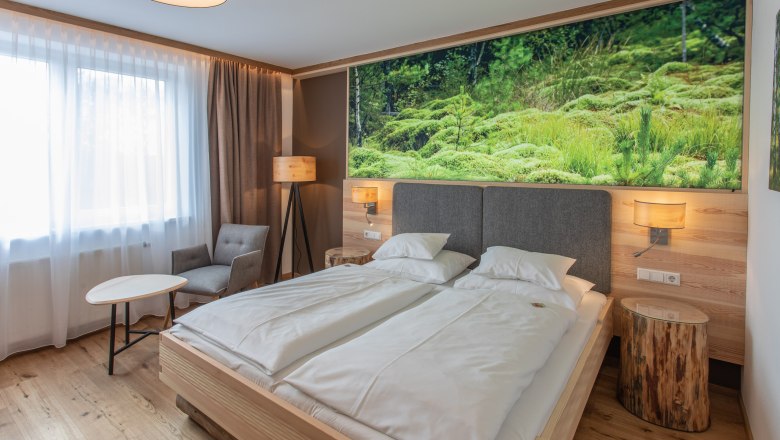 Modern hotel room with double bed, nature picture on the wall, armchair, table and floor lamp.