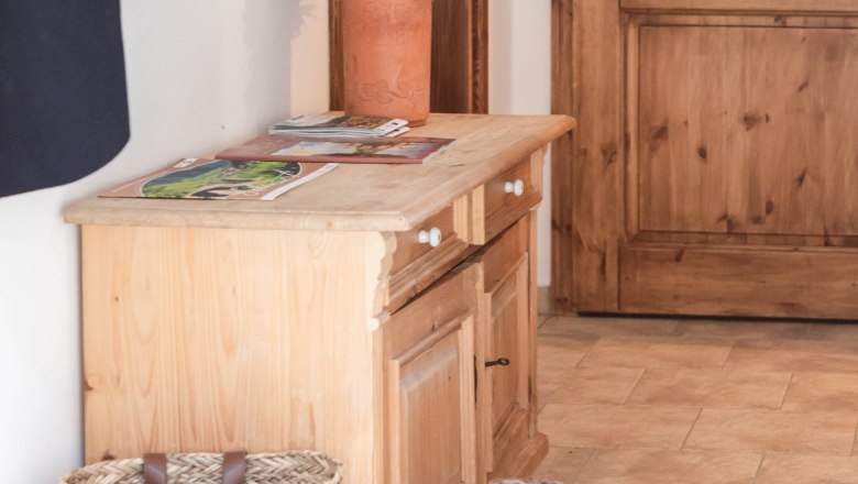 An anteroom with wooden furniture, a basket, boots and a vase of flowers.