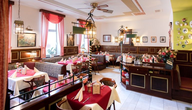 Interior view of a cozy pizzeria with red tablecloths and decorative lamps.