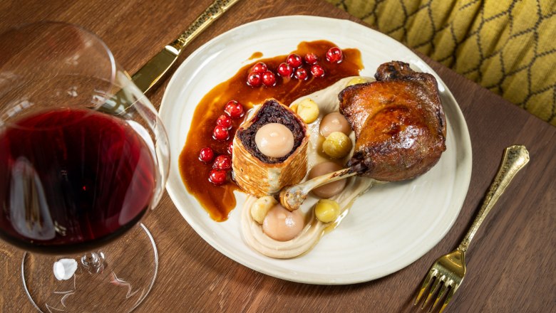 A plate with leg of goose, side dishes and red wine on a wooden table.