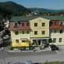 Yellow building with the inscription 'Gasthof Zur Alten Schule', surrounded by hills and trees.