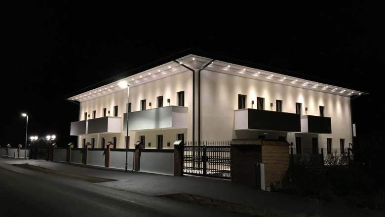 Illuminated building at night with balconies and streetlights.