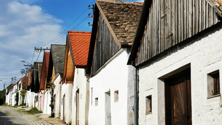 Row of wine cellars in Haugsdorf with red and gray roofs under a blue sky.