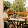 Two women playing cards on a balcony with a forest in the background.