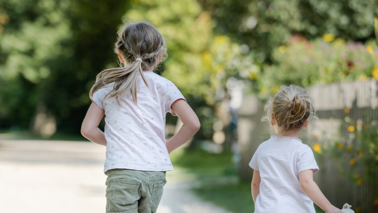 Two children running on a gravel path in a green park.