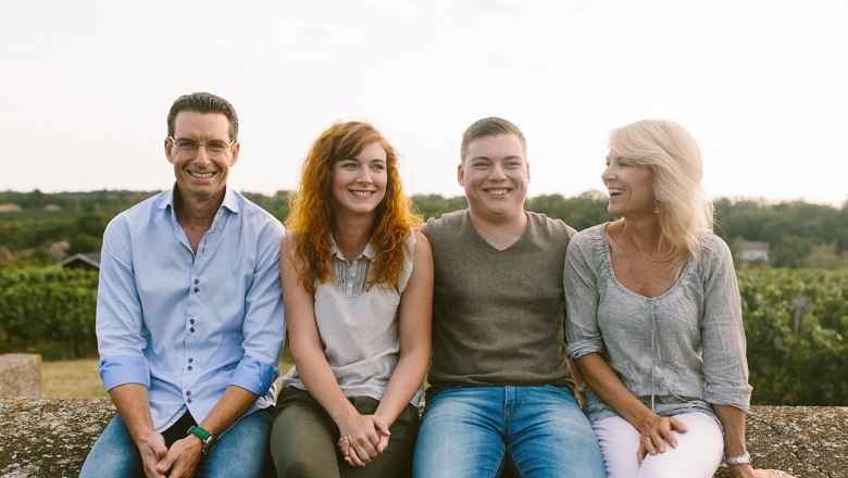 Four people sit smiling on a wall outside.