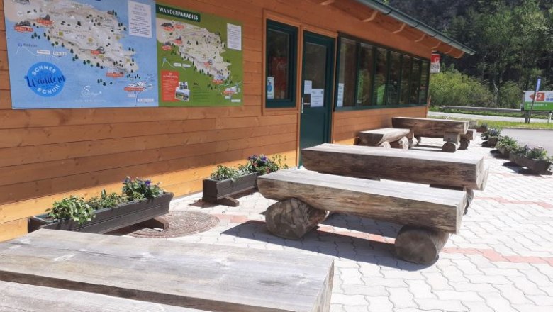 Wooden benches in front of a building with maps on the wall.