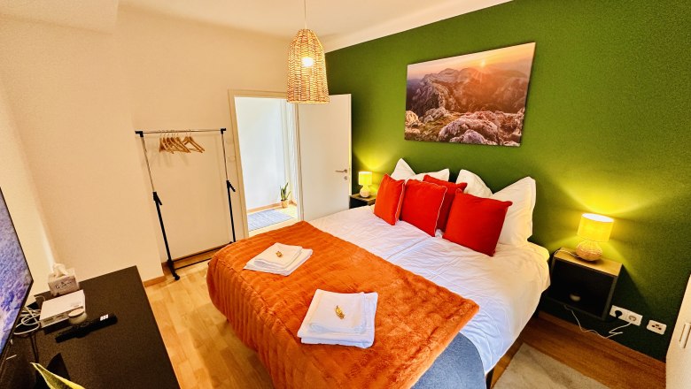 Cozy bedroom with green painted wall, double bed with red pillows, bedside tables and lamp.