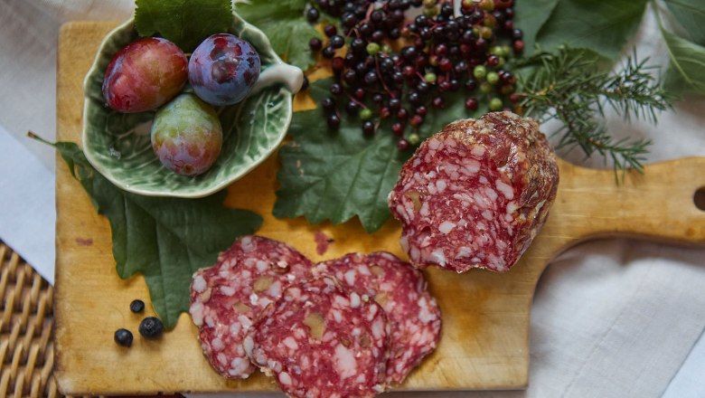 Close-up of a salami on a wooden board with berries and plums.