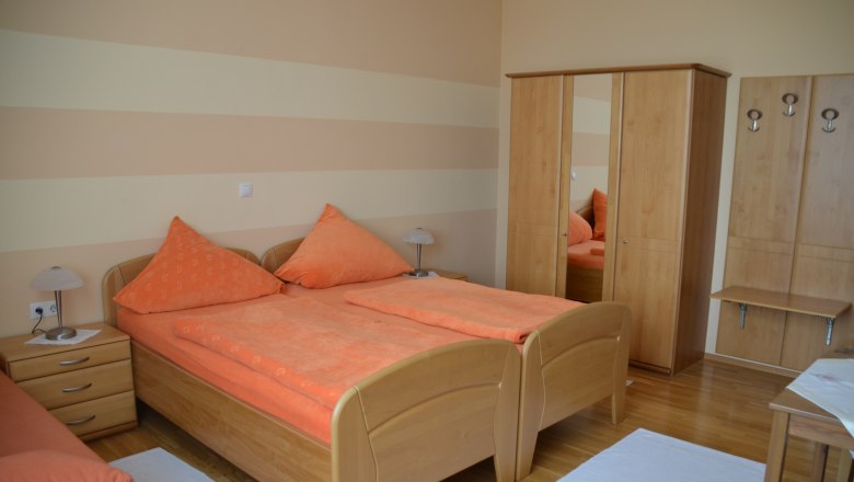 A cozy bedroom with two single beds, orange bed linen, a closet and bedside tables.