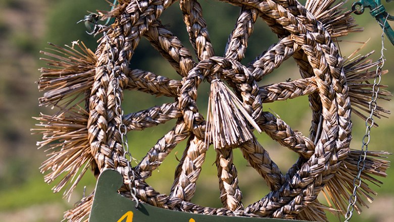 Woven straw wreath sign with the inscription "Ausg'steckt is'!" against a blurred background.