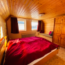 Wood-paneled bedroom with red comforter cover, two windows, a wardrobe and a bench.