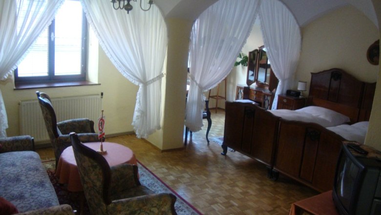 A cozy guest room with antique furniture, a double bed, armchairs and a small TV. Curtains separate the sleeping area.