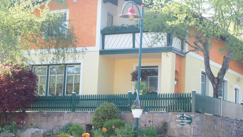 A two-storey house with an orange and yellow fa&ccedil;ade, green fence and garden.