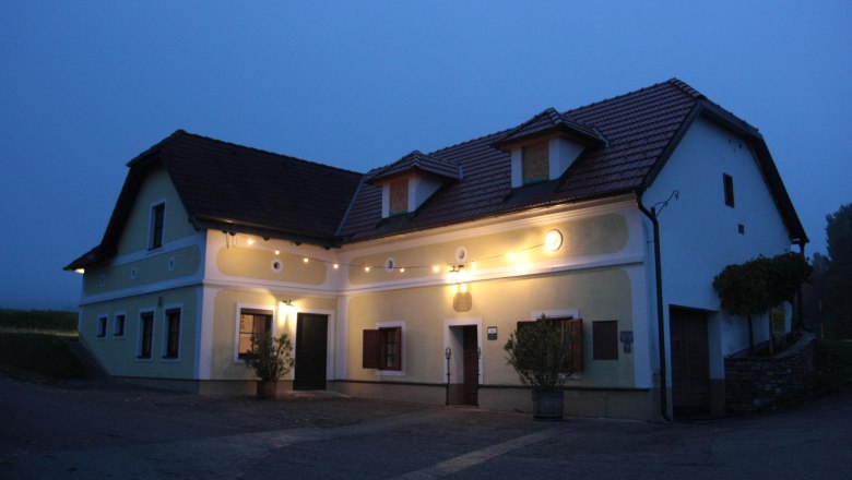 A traditional, illuminated house with a yellow fa&ccedil;ade and red roof tiles at dusk.