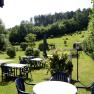 Garden with tables and chairs, surrounded by trees and meadows.
