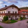 A traditional farmhouse with a red roof and balcony, surrounded by green countryside and trees.