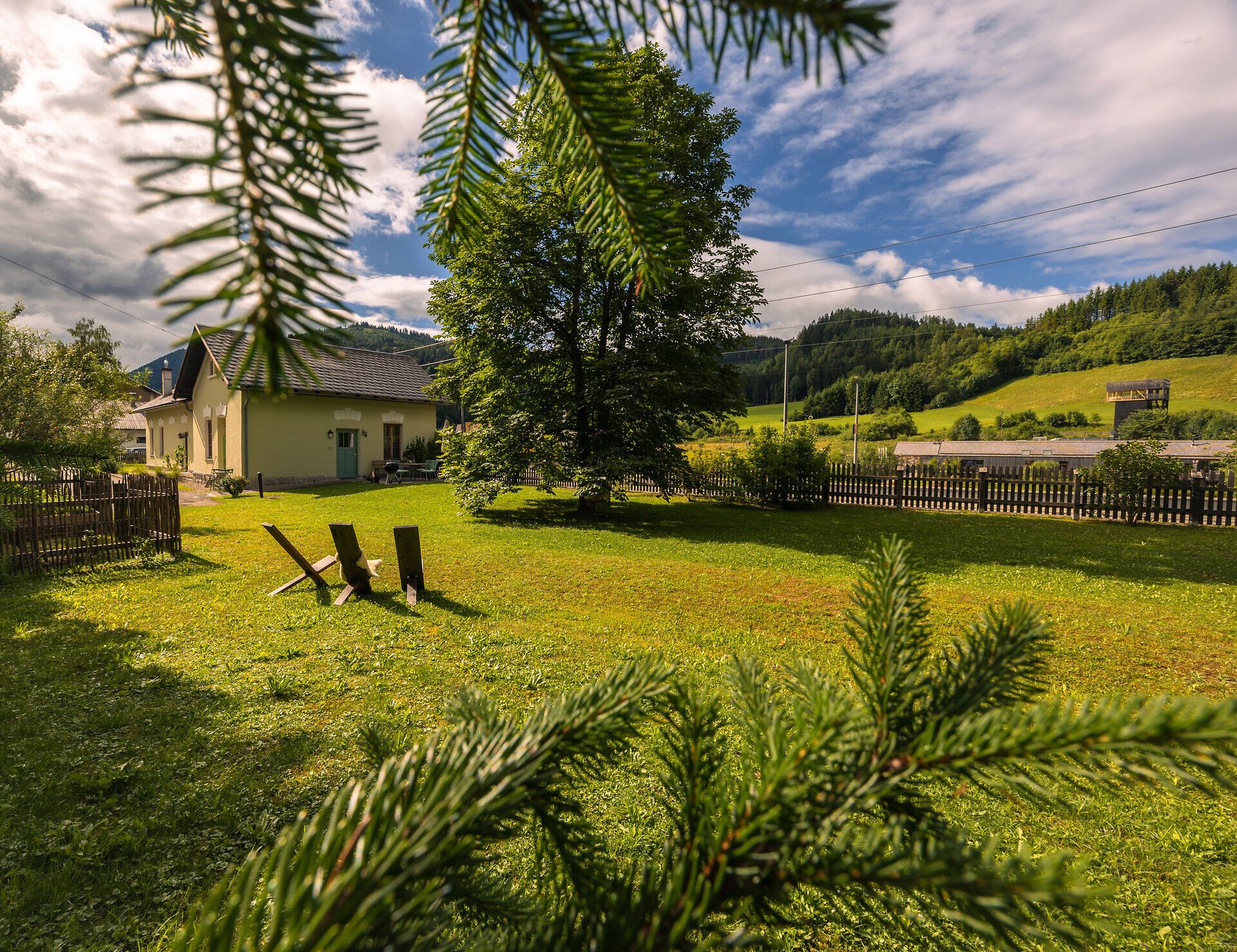 A golden train stops at Wienerbruck-Josefsberg station, surrounded by green countryside and a small outdoor seating area.