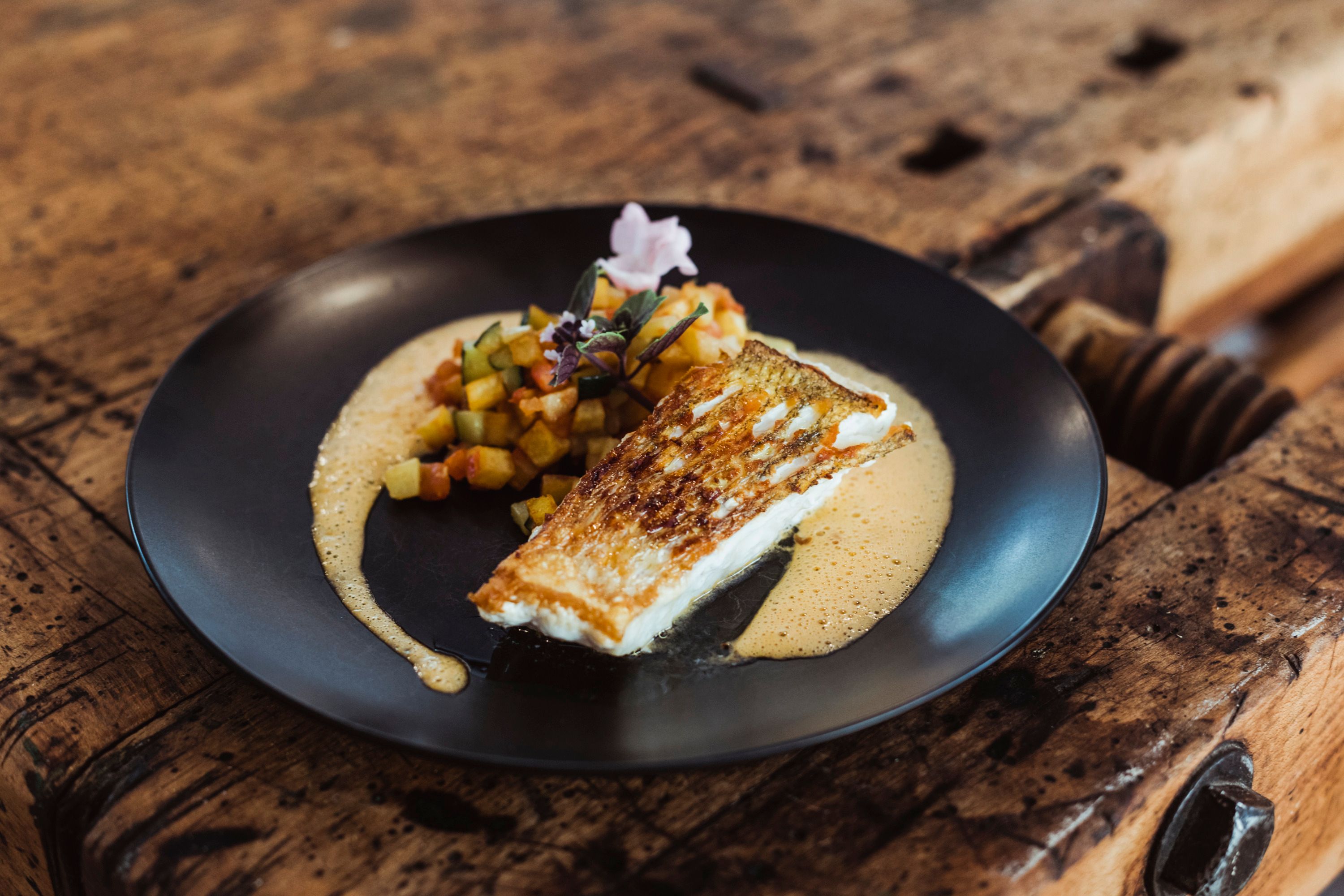 Fried fish with diced vegetables and sauce served on a black plate.