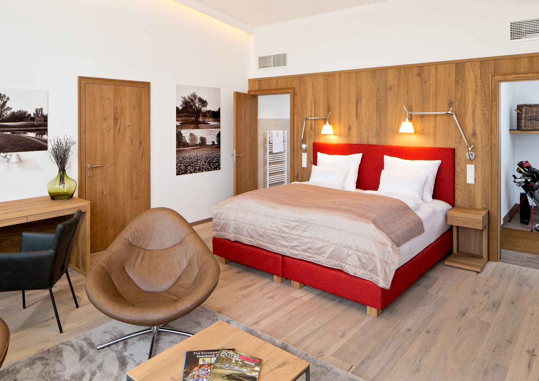 Modern hotel room with red bed, wooden furniture and golf magazines on the table.