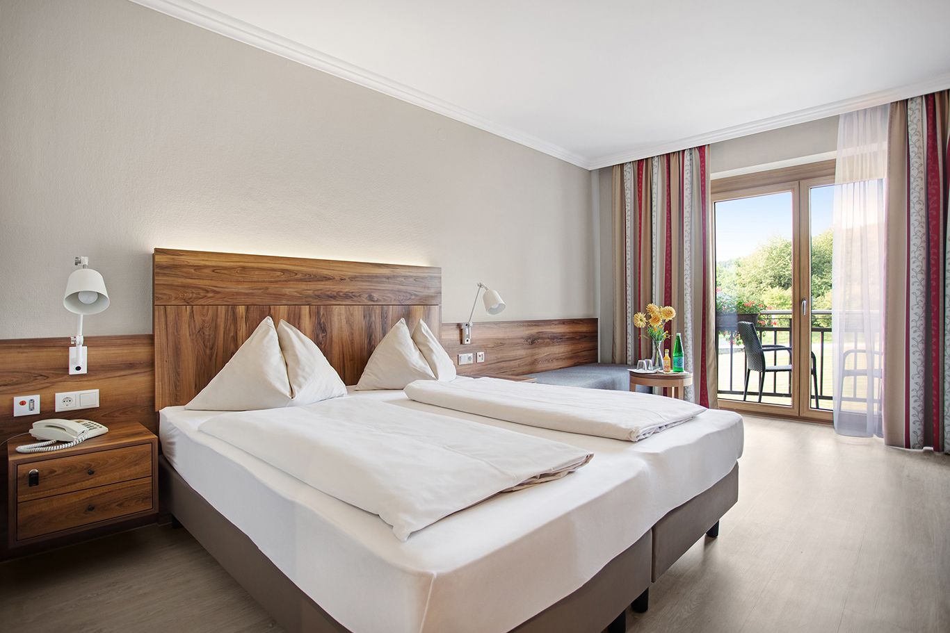 A cozy hotel room with a double bed, wooden furniture and a balcony with a view of the countryside.