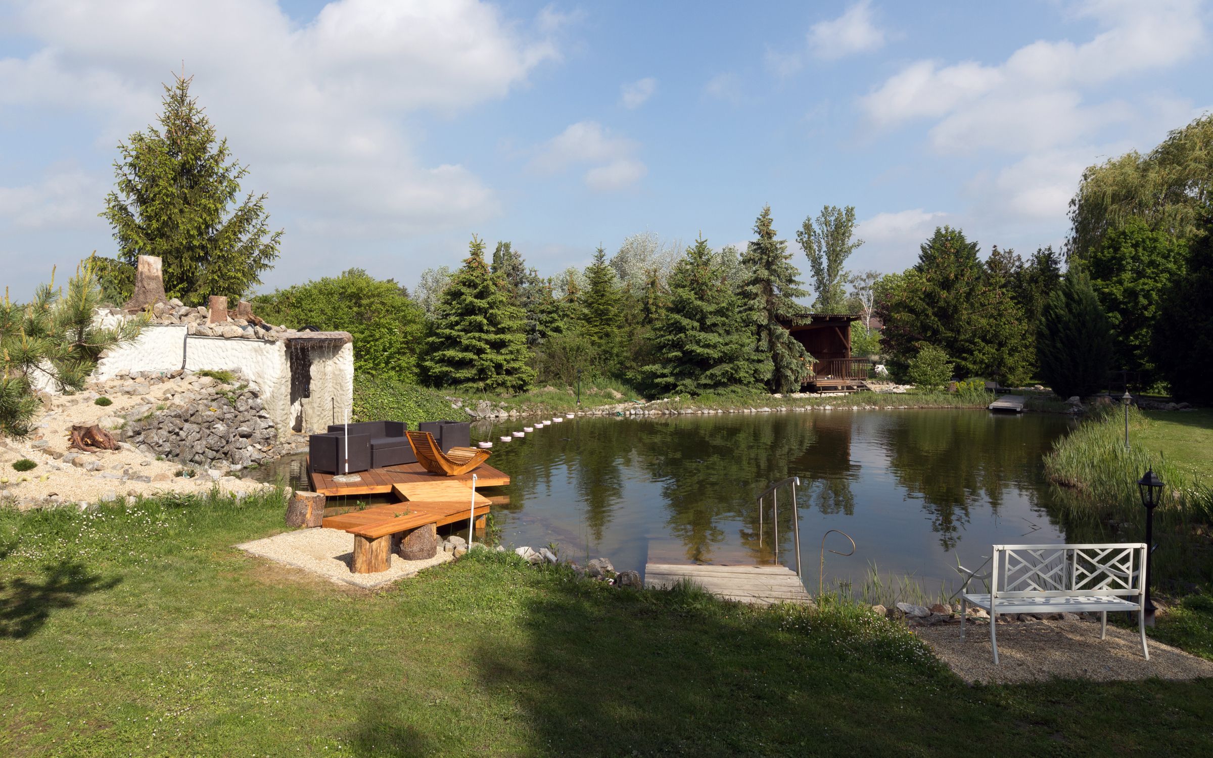 An idyllic garden pond with seating and surrounding vegetation.