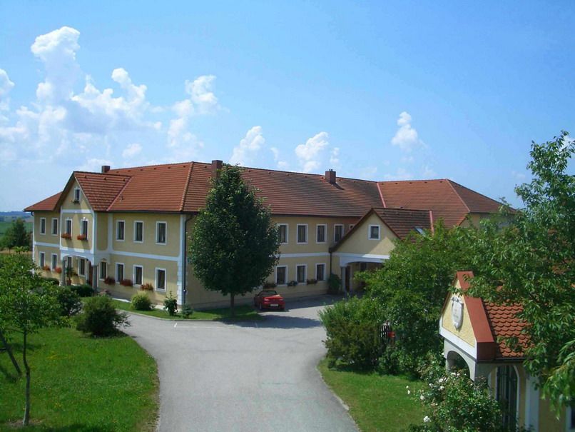Large farm with yellow walls and red roofs, surrounded by trees and a road.