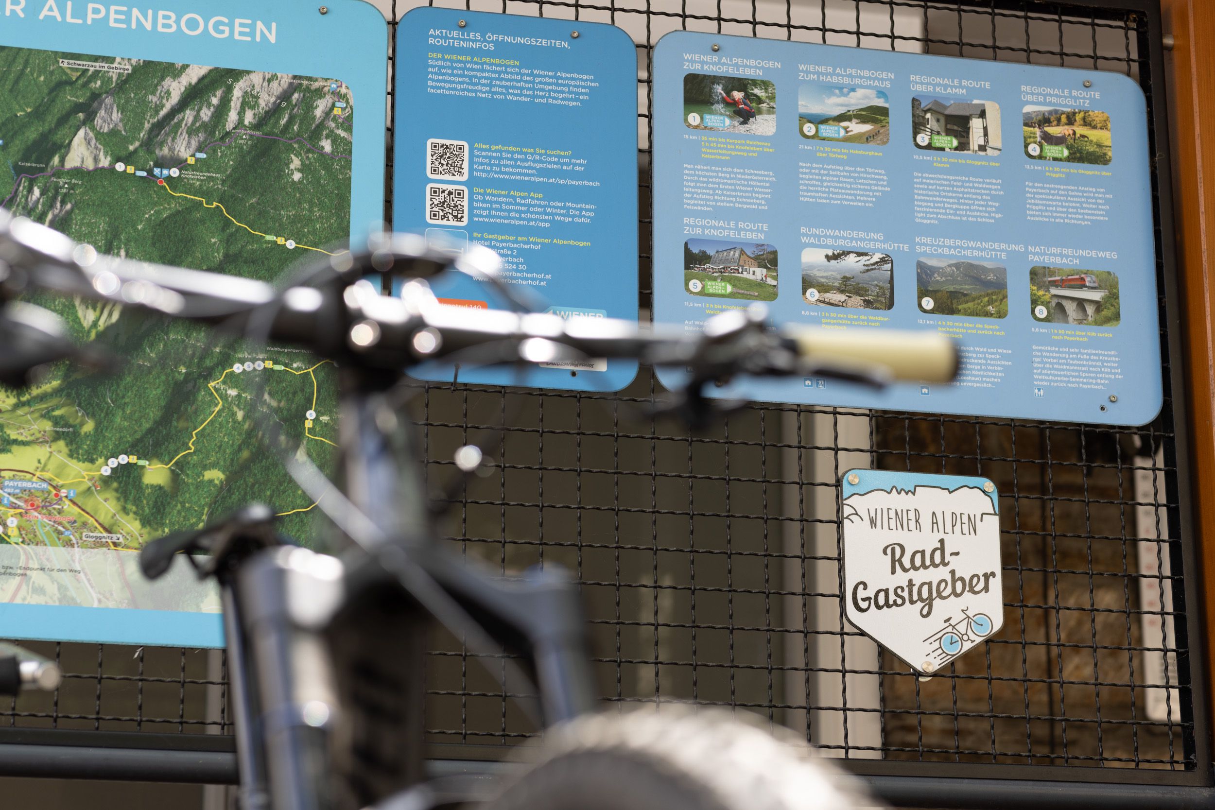 A bicycle stands in front of an information board with hiking and cycling trails in the Vienna Alps.