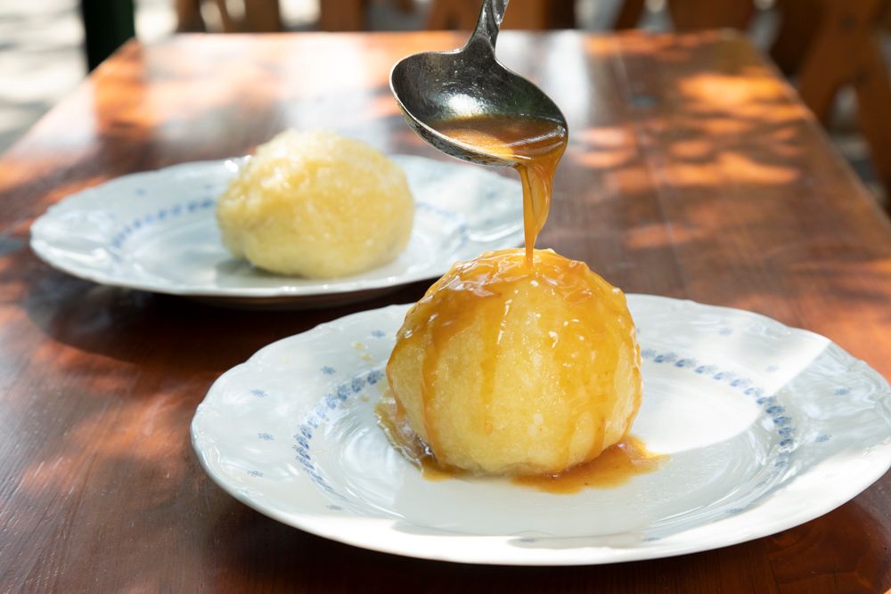 A dumpling on a plate is covered with sauce, another dumpling in the background.