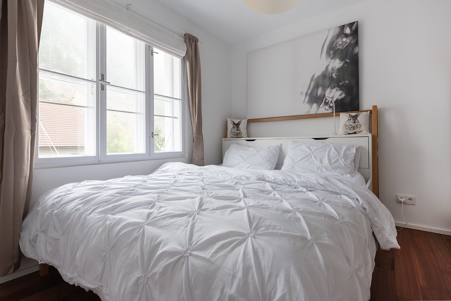Bright bedroom with a large bed, white bed linen and a large window with a view outside.