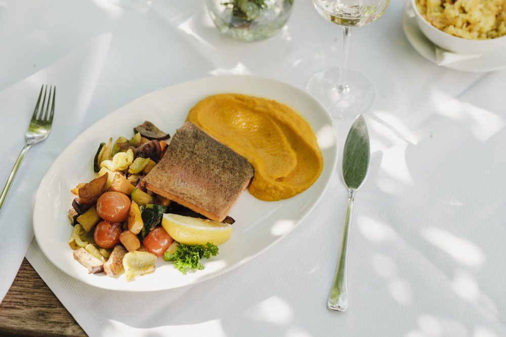 Set table with fish dish, vegetables and puree, white wine in the background.