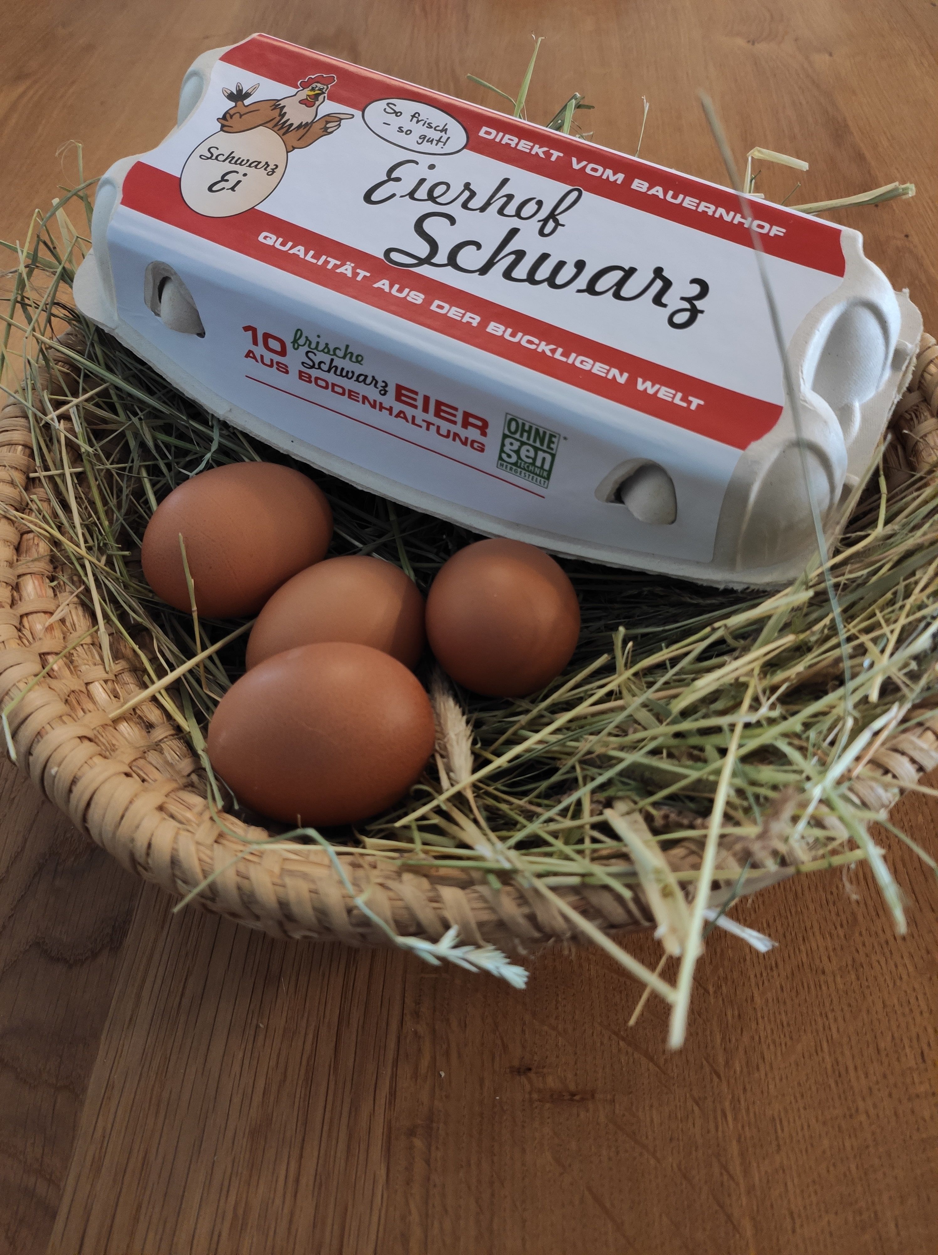 An egg carton labeled 'Eierhof Schwarz' lies on a basket of straw and brown eggs.