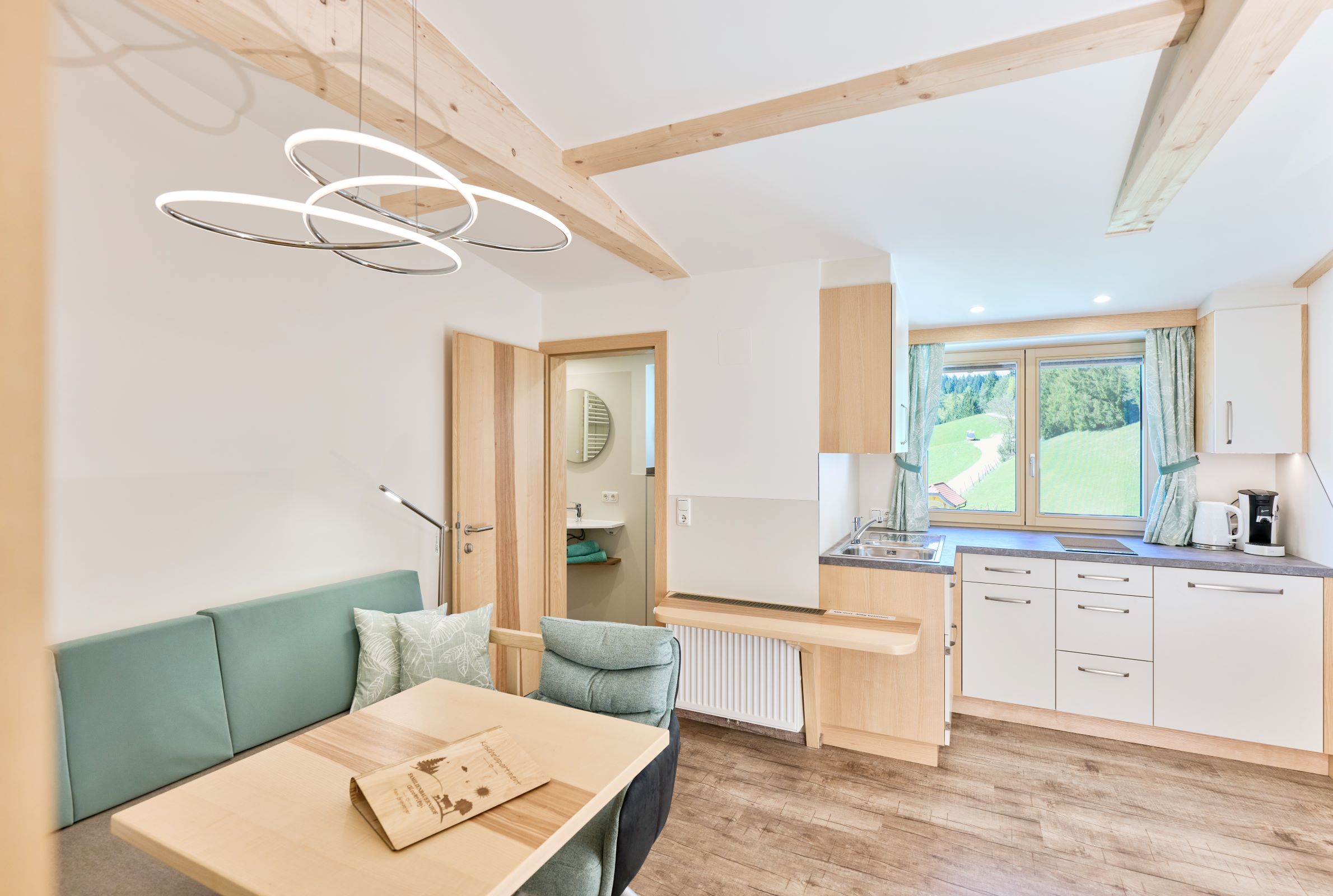Modern apartment with wooden elements, kitchenette and dining table. Windows with a view of the green landscape.