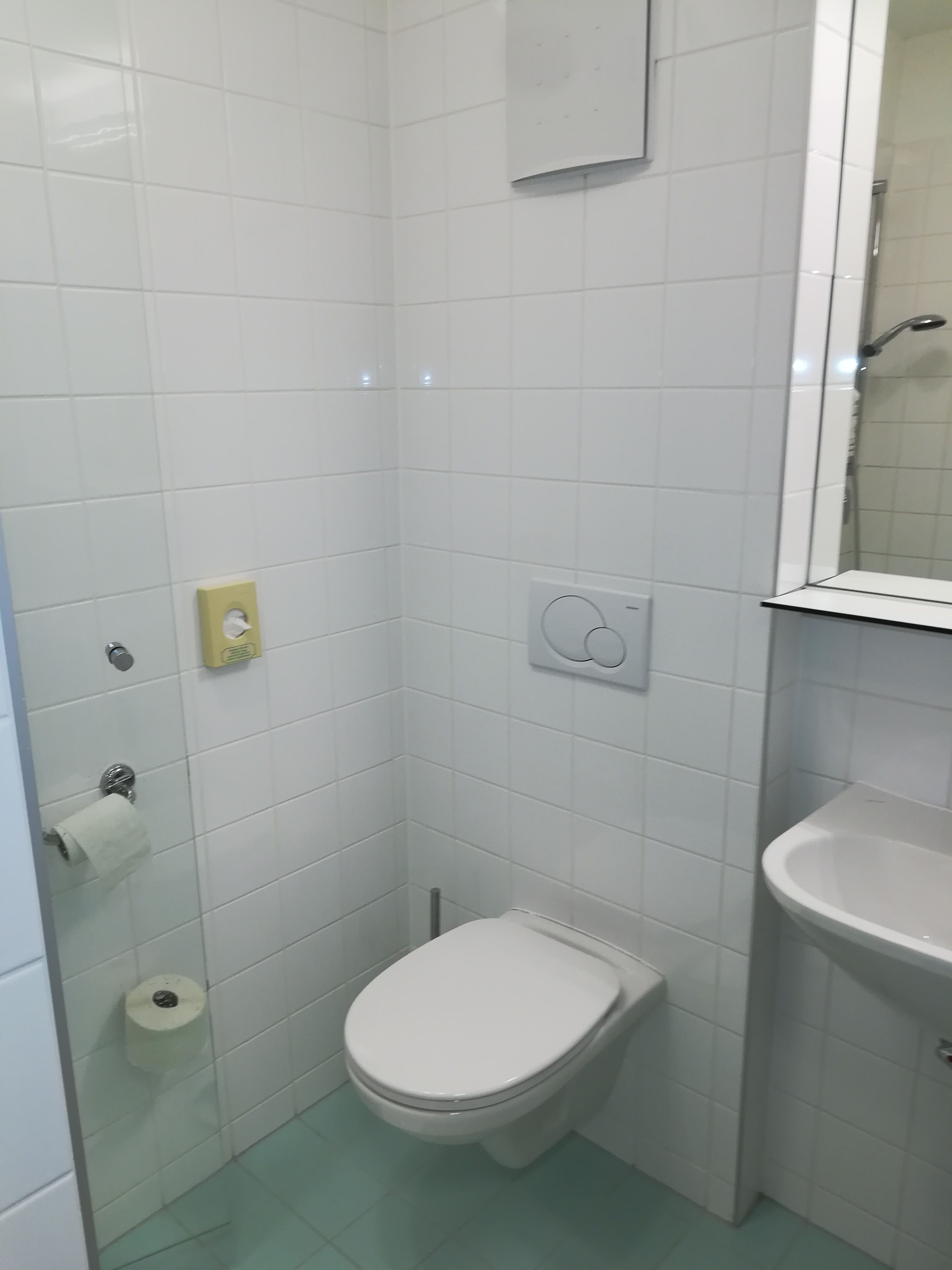 Small bathroom with white tiled walls, a toilet, washbasin and toilet roll holder.