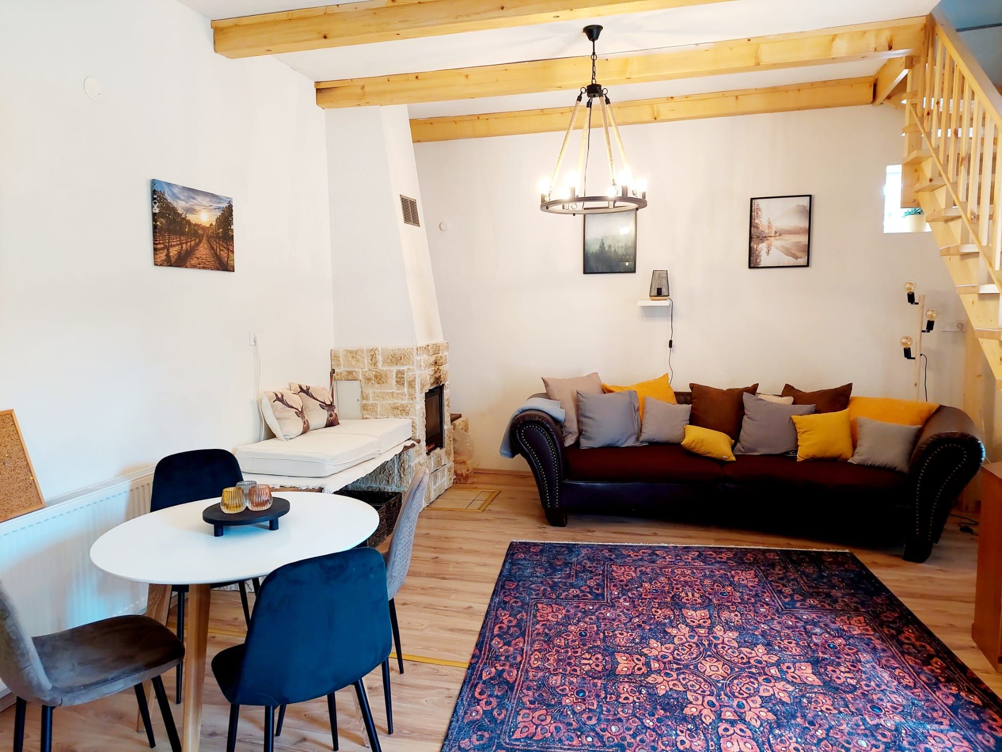 Cozy living-dining room with wooden beams, sofa, dining table and fireplace.