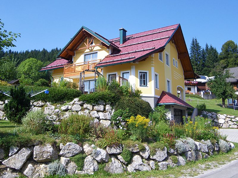 Yellow house with a red roof in a green landscape.