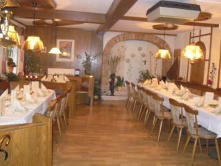 A cozy dining room with long, laid tables and wooden chairs, decorated with lamps and plants.