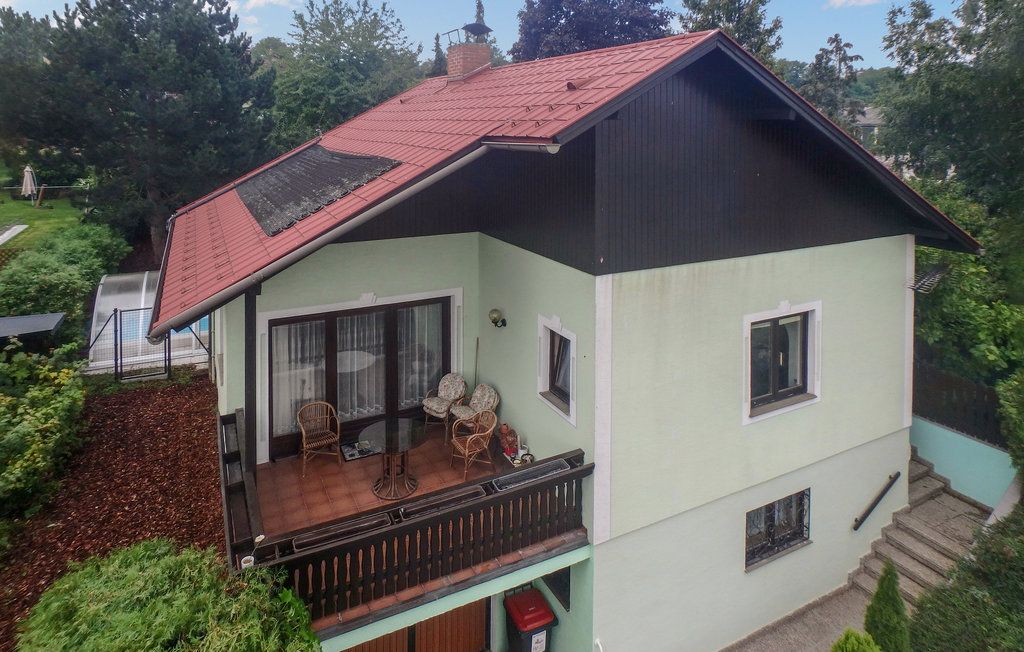 Two-storey house with red roof and balcony, surrounded by trees.