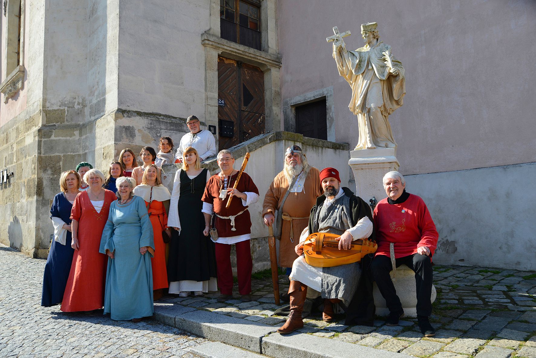Group of people in medieval clothing in front of a statue in an old town.