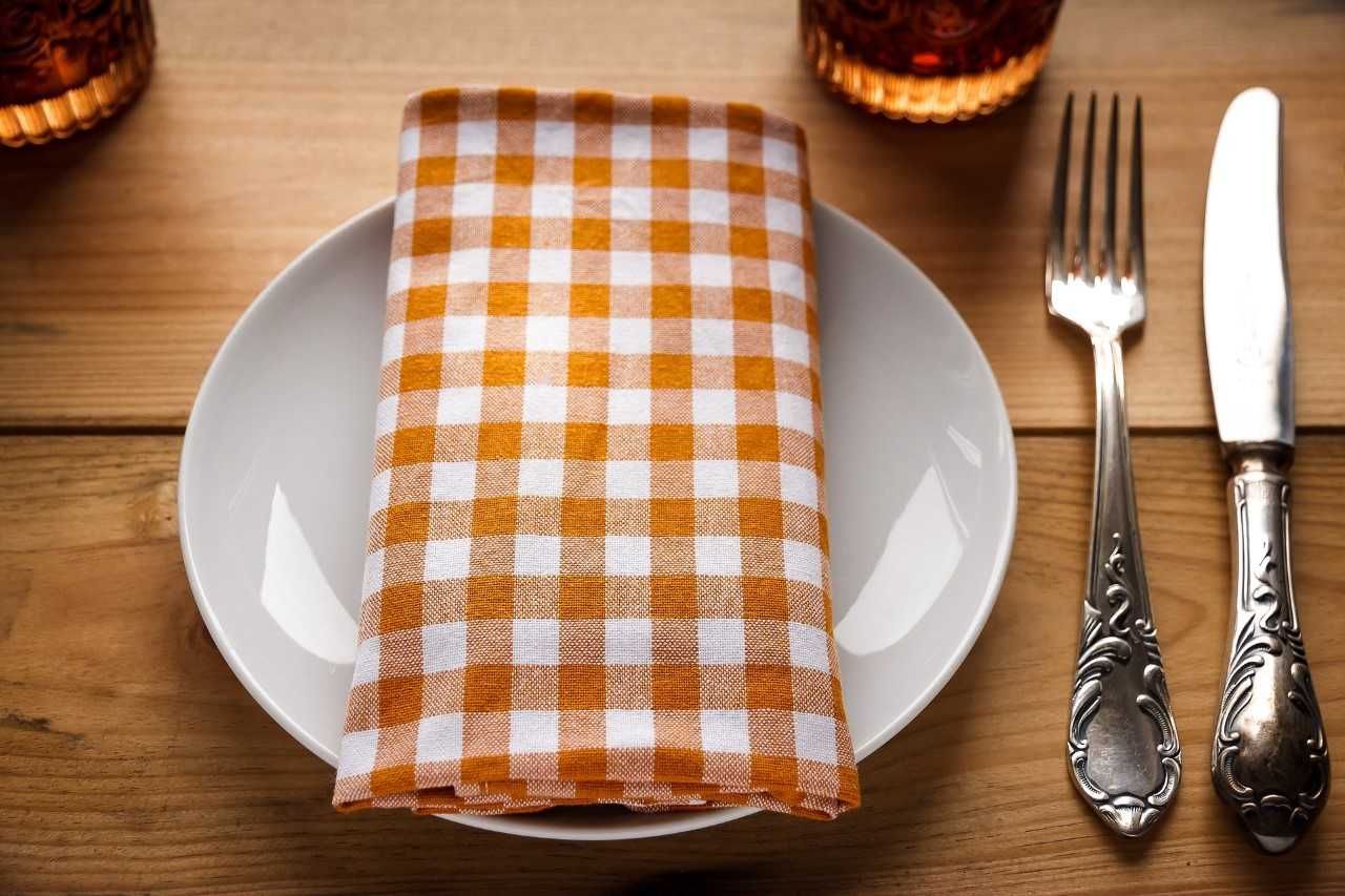 A plate with an orange and white checkered napkin, cutlery next to it on a wooden table.