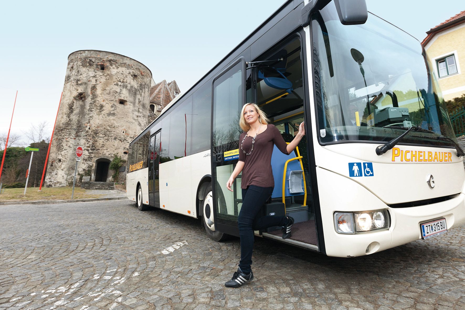 A woman gets off a bus in the Wachau, with a historic tower in the background.