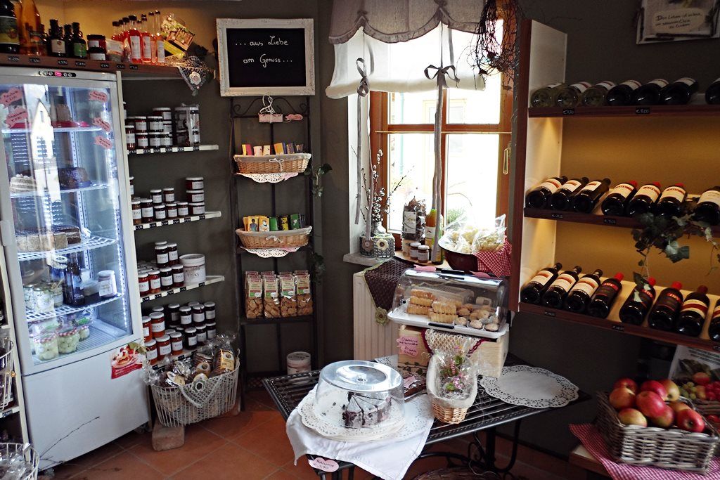 Interior view of a farm store with shelves full of bottles of wine, jams and pastries.