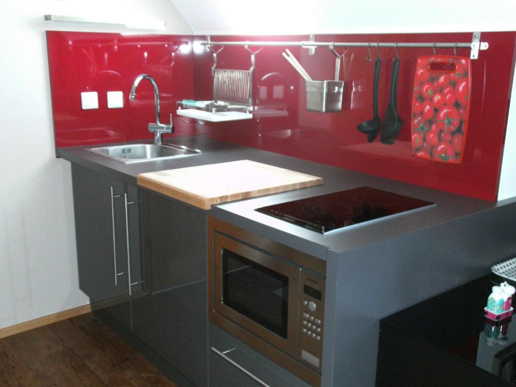 Modern kitchen with red splashback, sink, hob and microwave.