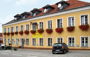 Yellow building with red flowers and cars in front of it.