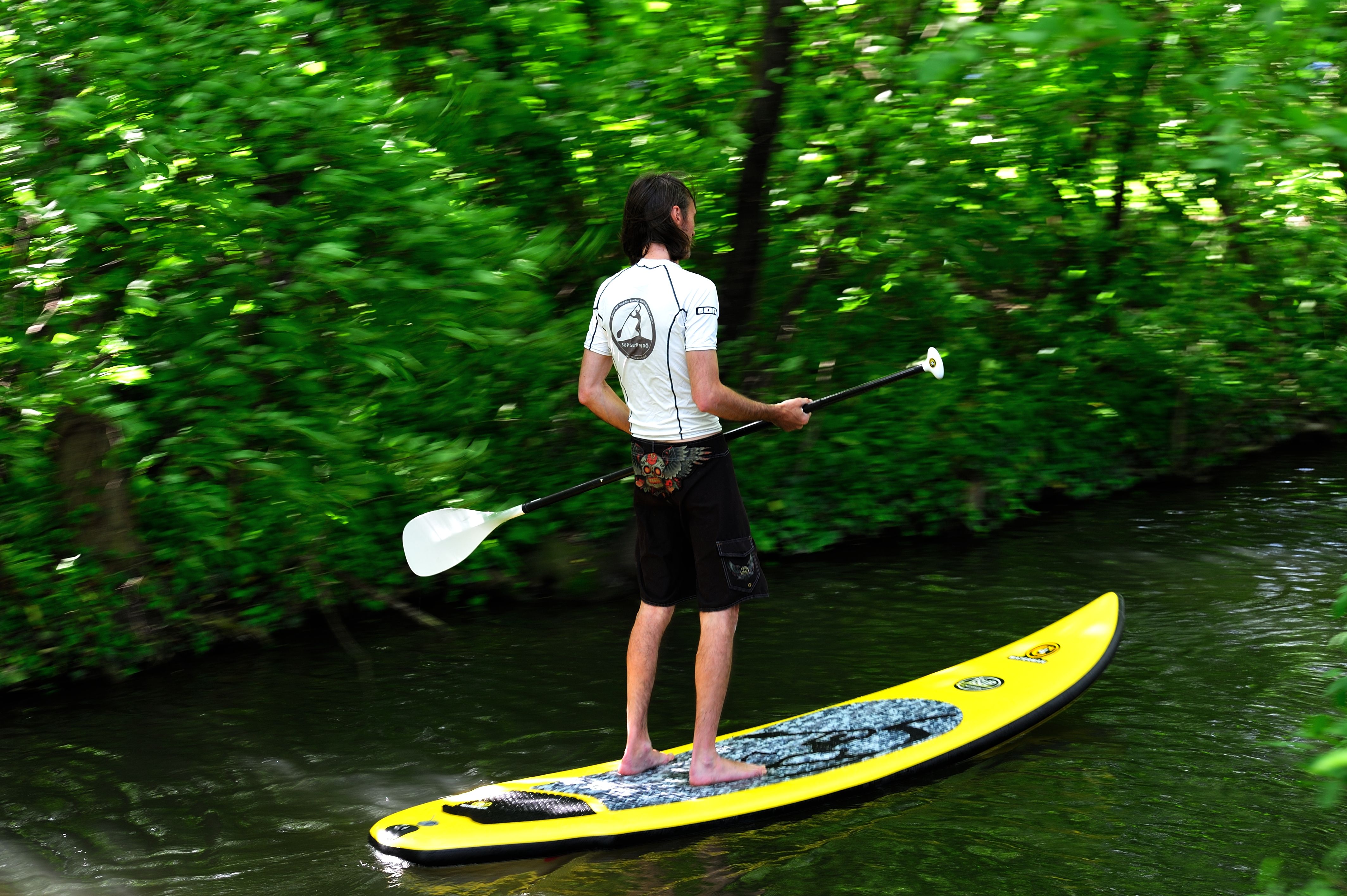 Person stand up paddling on a river, surrounded by green vegetation.